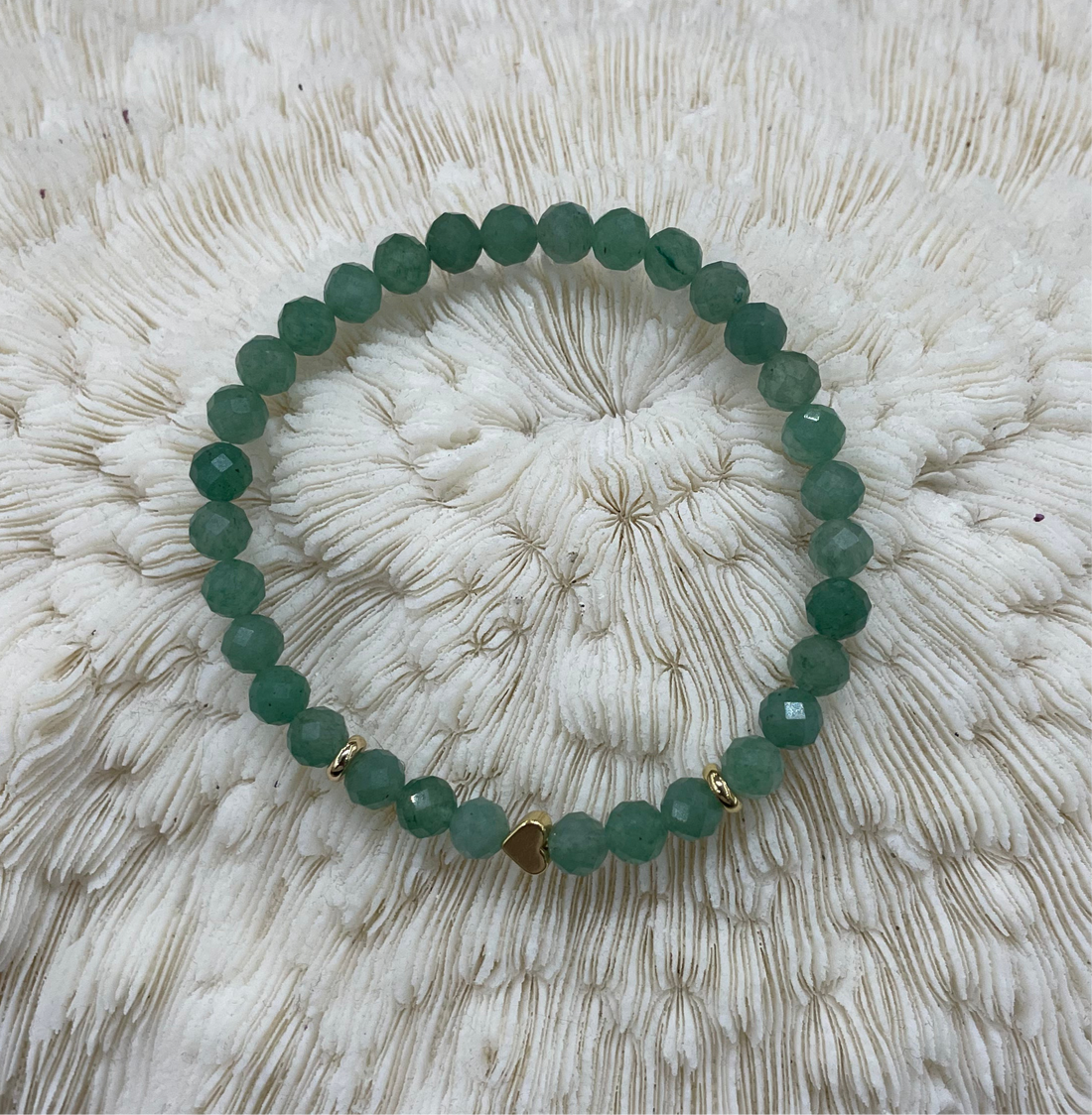 Green beaded bracelet with a gold heart charm on a textured white surface