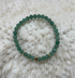 Green beaded bracelet with a gold heart charm on a textured white surface